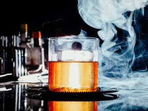 a front view iced drink inside little glass with smoke on the da