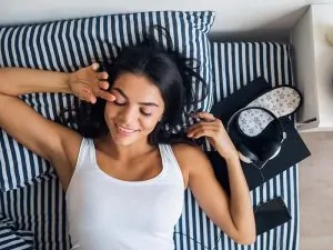portrait of young attractive woman lying in bed smiling, view from above, wake up in morning, lazy, leisure time, sunday, relaxing, breakfast, phone, headphones, book, sleeping mask